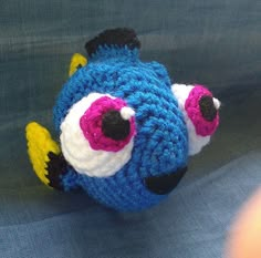 a crocheted blue fish with pink eyes and yellow fin on it's back