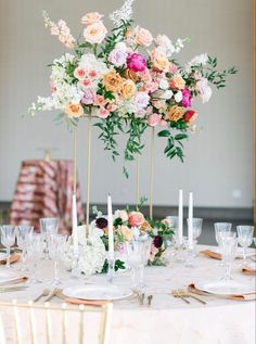 an arrangement of flowers and candles on a white table cloth with gold place settings in front of it