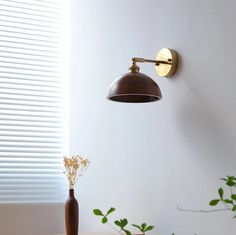 a wall light that is on the side of a wall next to a vase with flowers in it