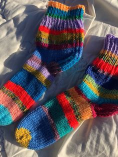 two pairs of colorful knitted socks laying on top of a white bed coverlet