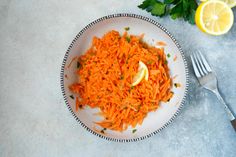 a white plate topped with shredded carrots next to a fork and lemon wedges