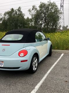 a blue and white convertible car parked in a parking lot next to yellow wildflowers