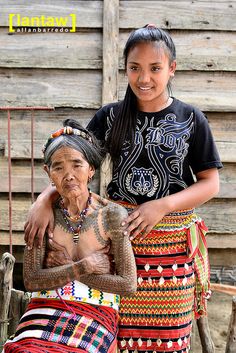 two women standing next to each other in front of a wooden building