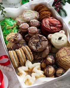 an assortment of cookies and pastries in a white box on a table next to christmas decorations