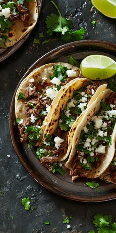 three tacos on a plate with limes and cilantro