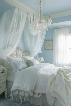 a white bed sitting under a chandelier in a bedroom next to a window