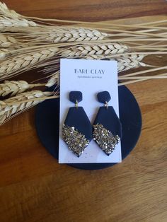 two pairs of earrings with gold glitter on them sitting on top of a wooden table