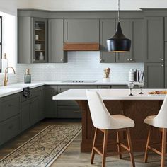 a kitchen with gray cabinets and white counter tops, two chairs at the center island