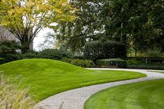 a lush green yard with white gravel and trees in the background, along with a path leading to a building