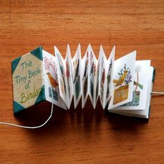 an origami book with cards attached to it sitting on a wooden table next to a string