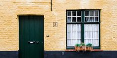 a yellow brick building with two green doors and window boxes on the outside, along with potted plants in front