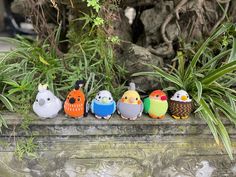 a row of small colorful birds sitting on top of a stone wall next to plants