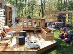 a wooden deck with chairs and tables in the grass next to an outdoor fireplace area