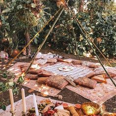 an outdoor picnic with bread and candles on the ground in front of trees, surrounded by greenery