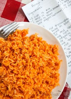 a white plate topped with rice next to a red checkered table cloth and a fork