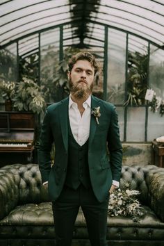 a man with a beard wearing a suit and bow tie standing in front of a couch