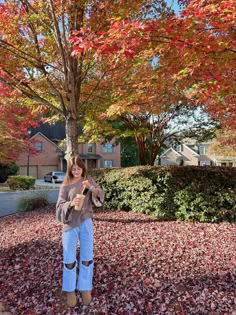 a woman standing in front of a tree with leaves on the ground