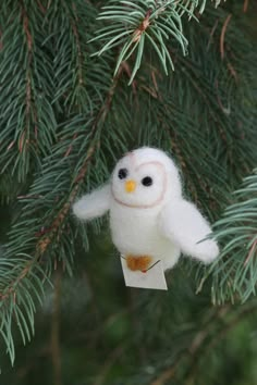 an ornament hanging from a pine tree with a small white owl on it