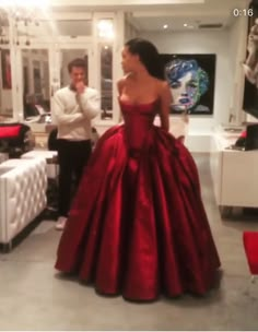 a woman in a red ball gown standing next to a man wearing a white shirt