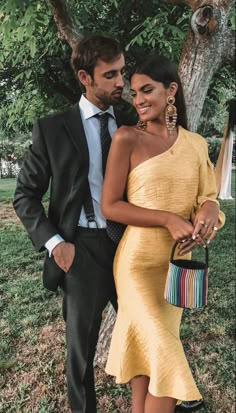 a man and woman standing next to each other in front of a tree wearing yellow dresses