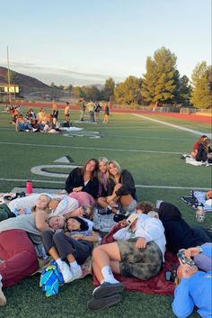 group of people laying on the ground in front of a football field at sunset with their arms around each other