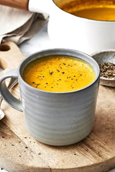 there is a bowl of soup on the table with spoons next to it and another bowl in the background