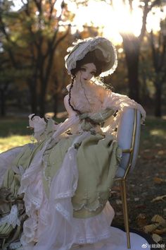 a doll sitting on top of a white chair in a park with trees behind it