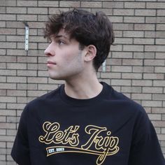 a young man standing in front of a brick wall wearing a black shirt that says let's trip