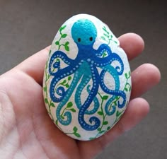 an egg decorated with blue and green octopus on it's shell is held in someones hand