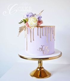 a white cake with gold drips and flowers on top is sitting on a stand