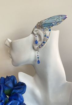 a white mannequin head with a blue flower and butterfly earring on it