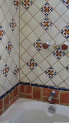 a bath tub sitting under a tiled wall next to a shower head and faucet