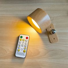 a remote control sitting on top of a wooden table next to a wall mounted light