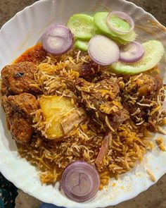 a white plate topped with rice and meat covered in onions, cucumbers and sauce