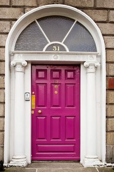 a bright pink door in front of a stone building with arched window and white columns