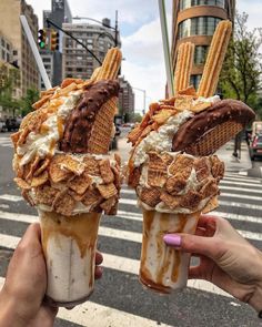 two ice cream sundaes are being held up