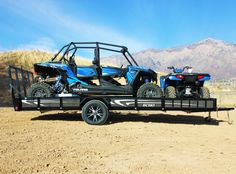 two atvs are parked on the back of a trailer in the middle of nowhere