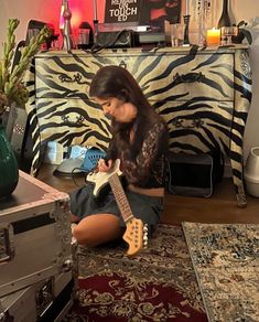 a woman sitting on the floor playing an electric guitar