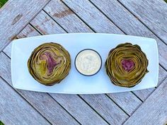 two artichokes on a white plate with a small dip in the middle