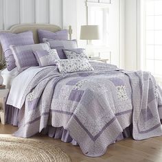 a bed covered in purple and white quilts