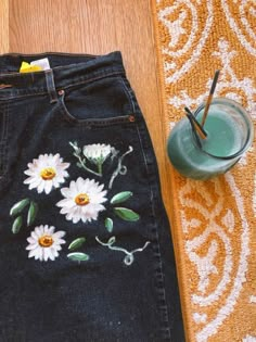 a pair of jeans with flowers painted on them next to a cup and strawberries