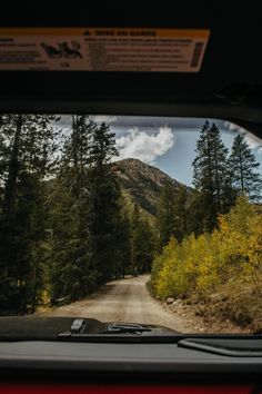 the view from inside a car looking at a road and mountains in the distance with trees on both sides