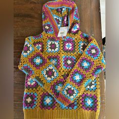 a colorful crocheted sweater with a hoodie attached to the front on a wooden floor