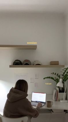 a woman sitting at a desk with a laptop computer in front of her and shelves above her