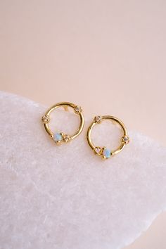 Brighten up your look with the Orbital Glow Opal Studs! These stunning studs feature man-made opal stones set in a 14k gold-plated circular design with sparkling cubic zirconia accents. The combination of opal and gold creates a timeless accessory that adds a touch of sophistication to any outfit. Why do we love these? They are super versatile and can work with every style and outfit! EARRINGS FEATURE Material: Brass, Man-Made Opal Stone Dimensions/Size: 8.5.mm Diameter, 1.1mm opal stone Finish: Gold Opal Jewelry, Minimalist Gold Earrings, Circular Earrings, Minimalist Earrings Gold, Studs Gold, Opal Earrings Stud, Circular Design, Opal Studs, Earrings Dainty