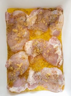 raw chicken in a white casserole dish with mustard and seasoning sprinkled on top