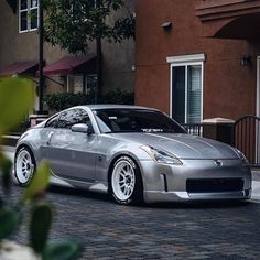 a silver sports car parked in front of a building on a brick road next to trees