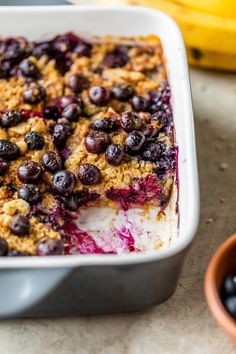 blueberry cobbler in a white baking dish next to a bowl of berries and bananas