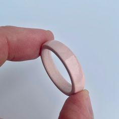 a hand holding a pink ring on top of a white surface with the finger pointing towards it