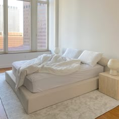 an unmade bed sitting in the middle of a room with a large window above it